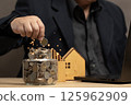 Man putting coins in a jar full of savings. The goal of real estate investing and using technology for financial management and informed decision making. Strategic planning and long term investment. 125962909