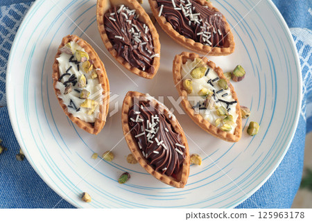 Sand dough tartlets with chocolate filling, pistachio nuts on white plate. Dessert for party, holiday.  125963178