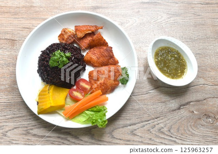 grilled slice pangasius dory fish on black riceberry with pumpkin carrot lettuce and tomato on plate dipping Thai spicy seafood sauce grilled slice pangasius dory fish on black riceberry with pumpkin carrot lettuce and tomato on plate dipping Thai spicy seafood sauce 125963257