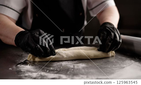 Chef rolling dough with rolling pin on stainless steel table 125963545