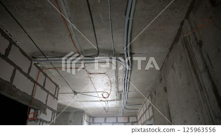 Construction site interior with electrical conduit installation on ceiling and brick walls 125963556