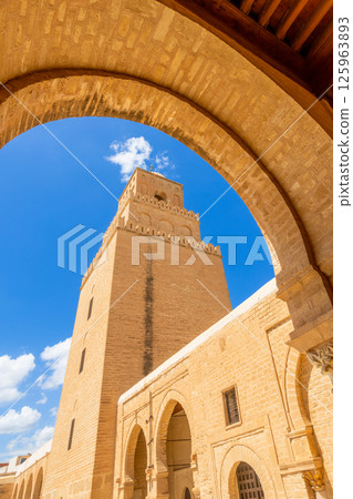 Arch view to minaret tower of the Great Mosque of Uqba with clouds in the blue sky, Kairouan 125963893