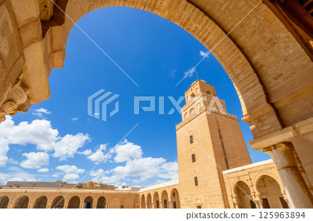 Arch view to minaret tower of the Great Mosque of Uqba with clouds in the blue sky, Kairouan, Tunis 125963894