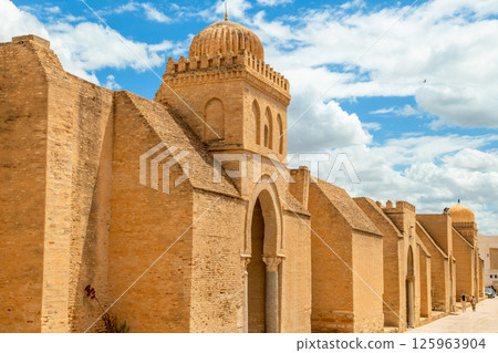 Ancient walls and dome of the Great Mosque of Uqba with clouds in the blue sky, Kairouan, Tunisia Ancient walls and dome of the Great Mosque of Uqba with clouds in the blue sky, Kairouan, Tunisia 125963904