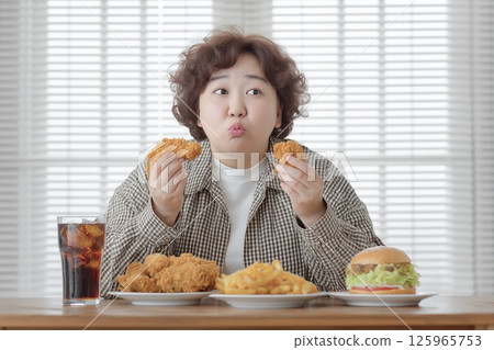 An obese woman looks satisfied surrounded by hamburgers, chicken, fries and coke An obese woman looks satisfied surrounded by hamburgers, chicken, fries and coke 125965753
