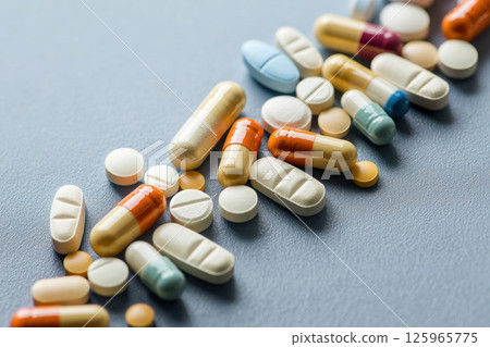 Pills and capsules in various colors and shapes on gray surface, symbolizing healthcare and wellness Pills and capsules in various colors and shapes on gray surface, symbolizing healthcare and wellness 125965775