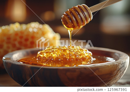 Golden honey drips from wooden dipper onto fresh honeycomb in rustic wooden bowl, showcasing artisanal beauty of natural sweetness 125967391
