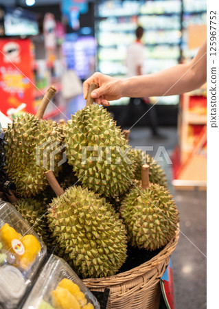 Choosing durian fruit. Shopper picks durian at outdoor Asian market examining texture and ripeness Choosing durian fruit. Shopper picks durian at outdoor Asian market examining texture and ripeness 125967752