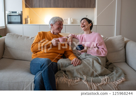 Laughing happy relaxed mature couple enjoying tea on couch while talking sharing during weekends 125968244