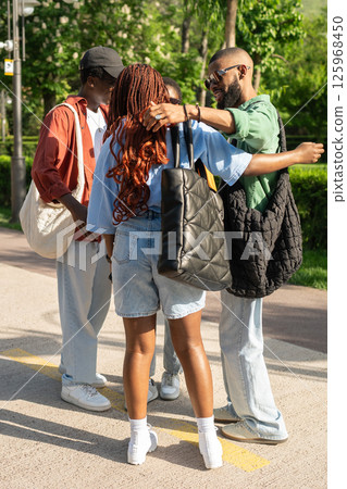 Excited happy group of African university students cheerfully greeting one another with hugs in park Excited happy group of African university students cheerfully greeting one another with hugs in park 125968450