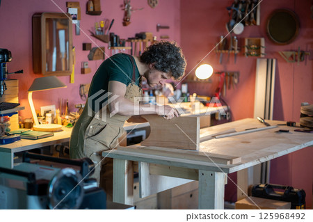 Carpenter meticulously assembles wooden furniture parts with precision on workshop workbench Carpenter meticulously assembles wooden furniture parts with precision on workshop workbench 125968492