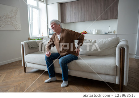 Sad depressed senior man suffering from osteochondrosis barely stand up from sofa, acute back pain Sad depressed senior man suffering from osteochondrosis barely stand up from sofa, acute back pain 125968513