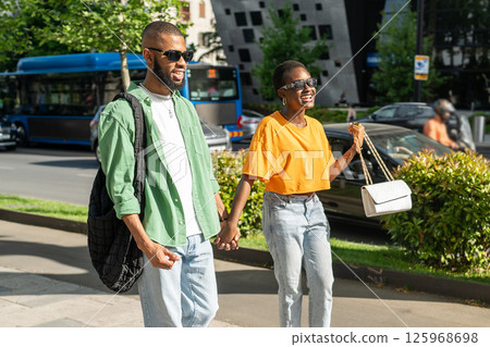 Playful fashionable African romantic couple stroll through city, chatting laughing and joking 125968698