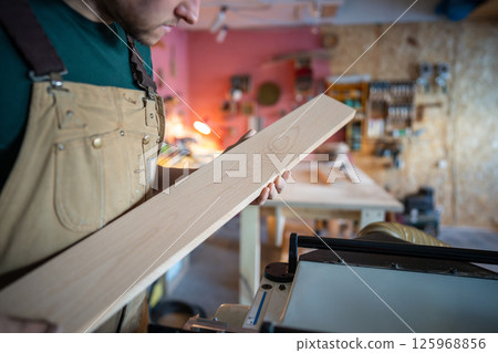 Concentrated attentive craftsman checking wooden plank carefully before crafting in carpentry Concentrated attentive craftsman checking wooden plank carefully before crafting in carpentry 125968856