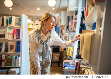 Enthusiastic woman selects books in bookstore alone. Book fair, book crossing, literature passion 125969116