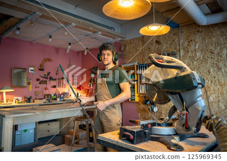 Confident skilled carpenter holding metal ruler preparing to work at woodworking station in workshop Confident skilled carpenter holding metal ruler preparing to work at woodworking station in workshop 125969345