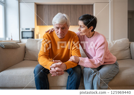 Sad frustrated mature couple sharing emotional struggle as wife consoles husband, life difficulties Sad frustrated mature couple sharing emotional struggle as wife consoles husband, life difficulties 125969440