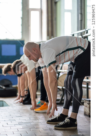 Determined rowers prepare for gym, stretching muscles, bending forward, activating flexibility 125969475