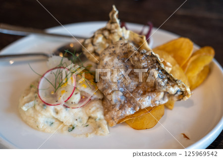 A close-up of crispy fried fish skin and potato chips, served with creamy salad and pickled red onions on plate 125969542