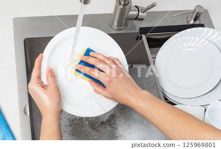 Housewife washing white plate with sponge in kitchen sink 125969801