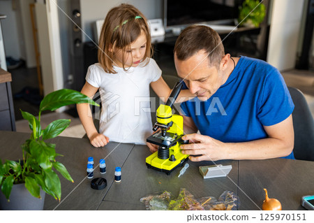 Father and daughter examining various plant samples under a microscope at home. Concept of family science education and botanical exploration Father and daughter examining various plant samples under a microscope at home. Concept of family science education and botanical exploration 125970151