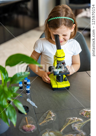 Little girl looking through a green microscope. Concept of curiosity and early scientific exploration 125970154