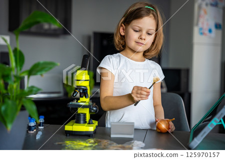 Little girl examining onion skin under a microscope. Concept of early science education and cell structure exploration Little girl examining onion skin under a microscope. Concept of early science education and cell structure exploration 125970157