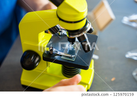 Close up view of hands of man examining various samples under a microscope at home as a hobby. Concept of scientific curiosity and amateur microscopy Close up view of hands of man examining various samples under a microscope at home as a hobby. Concept of scientific curiosity and amateur microscopy 125970159