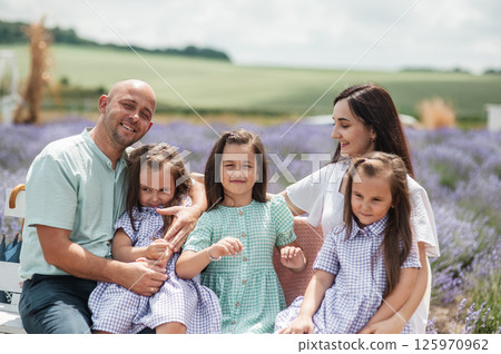 A family sits on a bench in the middle of a lavender field.  125970962