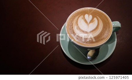 close up of a flat white coffee with a floral coffee art in a blue cup on a dark brown background with copy space 125971405