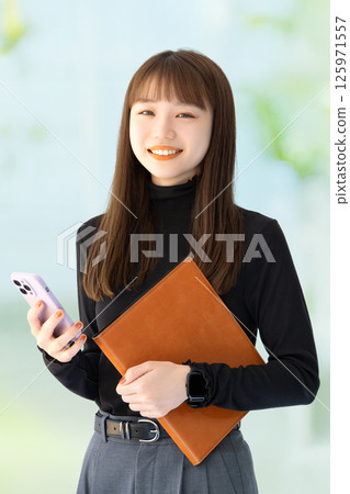 Smiling female businesswoman holding a smartphone and a binder Smiling female businesswoman holding a smartphone and a binder 125971557