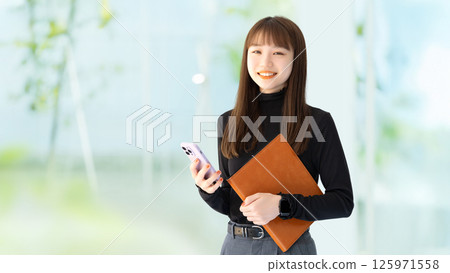Smiling female businesswoman holding a smartphone and a binder 125971558