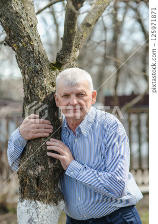 A pensioner in a spring garden. An old man leaning against a tree. A pensioner in a spring garden. An old man leaning against a tree. 125971871