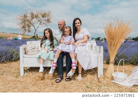A happy family on a beautiful lavender field. An interesting conversation of a young family with little daughters on a purple field. A happy family on a beautiful lavender field. An interesting conversation of a young family with little daughters on a purple field. 125971901