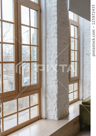 Large windows with wooden frames in loft interior with white brick walls inside apartment or house 125972435