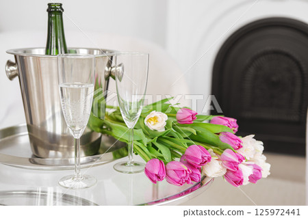 Champagne and sparkling glasses and bouquet of pink and white tulips in white modern living room 125972441
