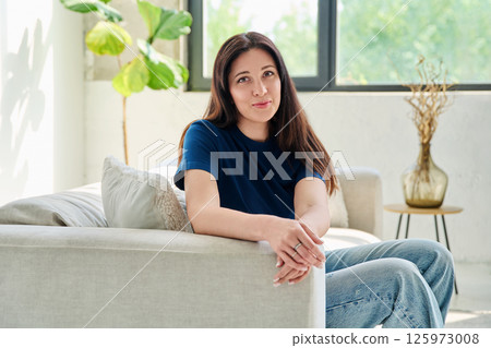 Portrait of beautiful young brunette woman sitting on sofa in living room Portrait of beautiful young brunette woman sitting on sofa in living room 125973008