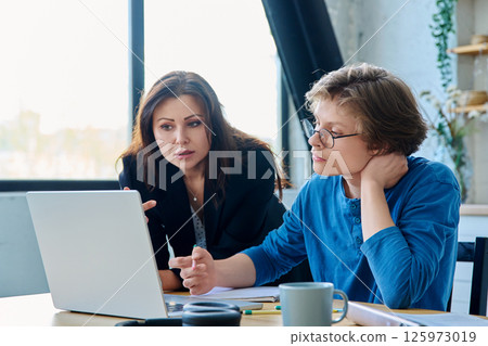 Teenage boy student with female mentor trainer teacher looking at laptop computer screen 125973019