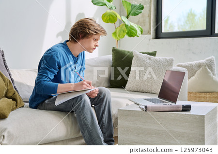 Teenager guy student studying sitting at home on sofa using laptop textbook notebook Teenager guy student studying sitting at home on sofa using laptop textbook notebook 125973043