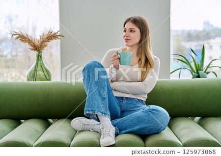 Portrait of relaxed beautiful young woman sitting at home on sofa with cup Portrait of relaxed beautiful young woman sitting at home on sofa with cup 125973068