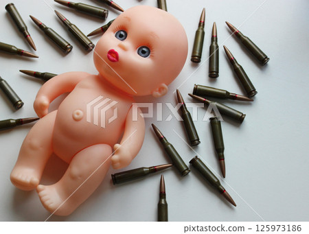 Bullets Scattered Around Naked Doll As Symbol Of Childs Victims Of War. Naked doll lying on a scattered on white surface bullets top view 125973186