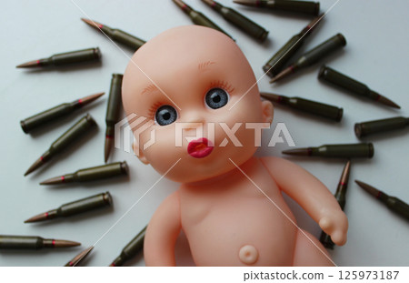 Sad Sight Of Toy Doll Over Ammunition Cartridges. Conceptual Photo On The Topic Of Children Killed In War 125973187
