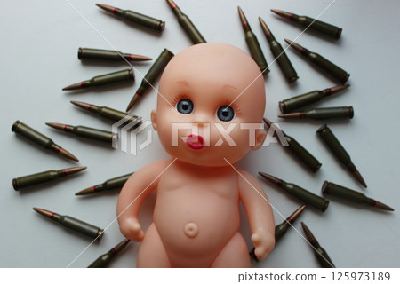 Lost Childhood Concept Photo. Naive face of a child's doll lying on a bullets top view. Sad Sight Of Toy Doll On Clean Surface With Scattered Bullets Lost Childhood Concept Photo. Naive face of a child's doll lying on a bullets top view. Sad Sight Of Toy Doll On Clean Surface With Scattered Bullets 125973189