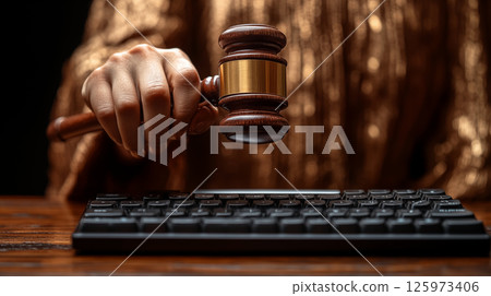 Wooden gavel hovering over computer keyboard closeup, digital law concept 125973406