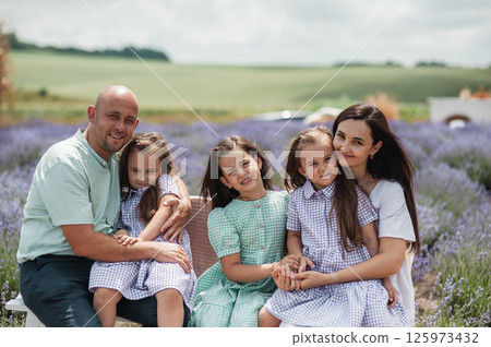 A family rests on a wooden bench in the middle of a lavender field. A family rests on a wooden bench in the middle of a lavender field. 125973432
