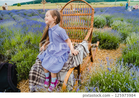 A girl with long, loose hair and a purple dress is sitting in a rocking chair in a lavender field. A girl with long, loose hair and a purple dress is sitting in a rocking chair in a lavender field. 125973984