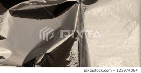 Silver foil with shiny, metallic texture creates a smooth, reflective surface. Crinkled and folded 125974064