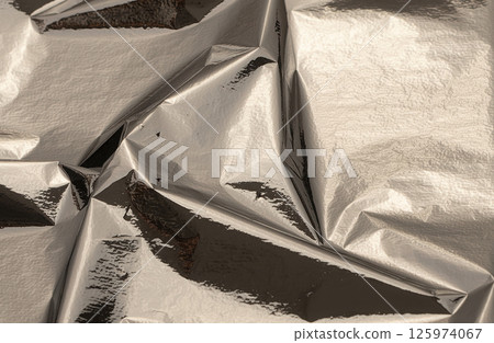 Silver foil with shiny, metallic texture creates a smooth, reflective surface. Crinkled, folded Silver foil with shiny, metallic texture creates a smooth, reflective surface. Crinkled, folded 125974067