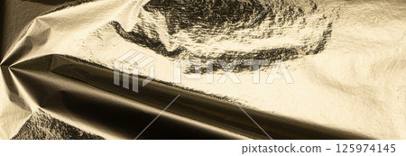 Gold metallic foil texture with a crumpled, folded surface. Shiny, glossy material reflecting light 125974145
