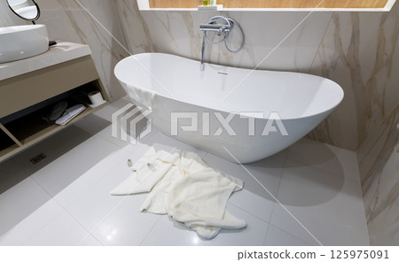 A modern freestanding bathtub in a luxury bathroom with towels left on the floor A modern freestanding bathtub in a luxury bathroom with towels left on the floor 125975091